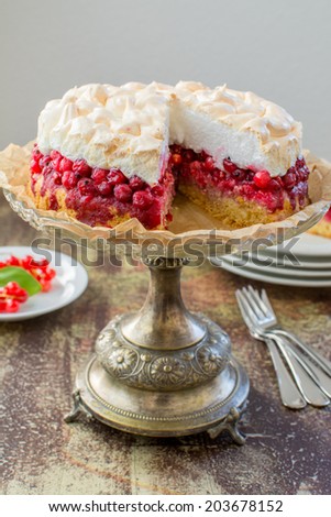 Red currant meringue tart on a vintage cake stander, a stack of white dishes, Dessert forks and a plate of fresh red currants on a vintage painted surface