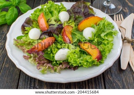 Close-up of assorted salad leaves, grilled peaches and mozzarella salad on a white vintage plate placed on a dark wooden surface