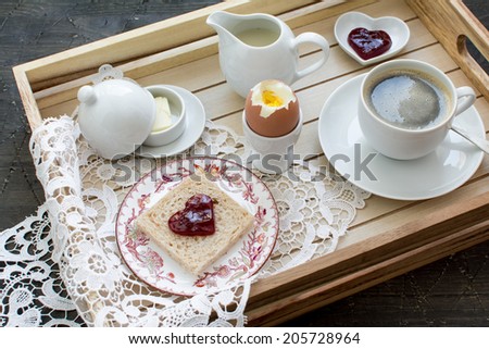 Breakfast on a tray: a cup of coffee, a whole grain toast, marmalade, egg, butter and milk.