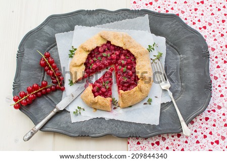 Closeup of homemade red currants galette on a serving plate placed on a natural wood surface covered with red white cloth