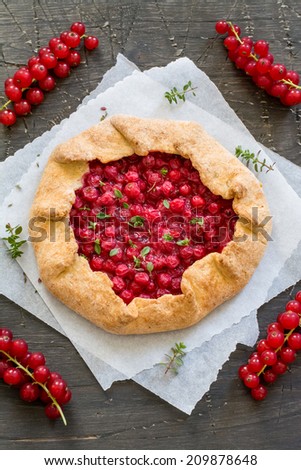 Fresh baked galette with red berries, thyme and red currants on a natural dark wood surface covered with baking paper
