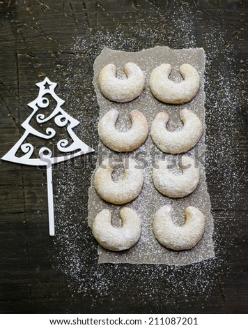 Sugar powdered vanilla crescents and a christmas tree decoration on a natural dark wood surface covered with baking paper