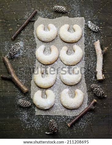 Sugar powdered vanilla crescents christmas cookies on a dark wood surface covered with baking paper; christmas decoration around