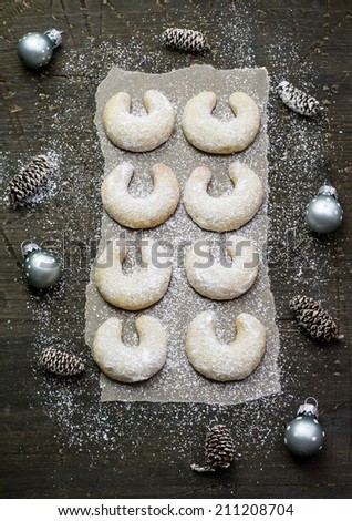 Sugar powdered vanilla crescents christmas cookies on a dark wood surface covered with baking paper; christmas decoration around
