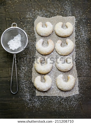 Sieve and sugar powdered vanilla crescents christmas cookies on a dark wood surface covered with baking paper