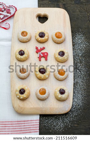 Thumbprint cookies with raspberry and apricot jams on a wooden serving board placed on a natural dark wood surface covered with the white red tea towel