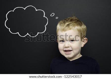 Smart young boy wearing a navy blue jumper stood in front of a blackboard with a drawn on chalk thought bubble