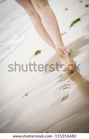 Close up of a woman\'s legs walking along the beach as the tide comes in