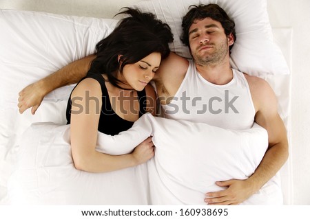 Beautiful couple laid asleep cuddling in the morning in a white bed