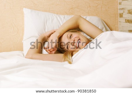Close up of a smiling cute woman lying under sheet in bedroom