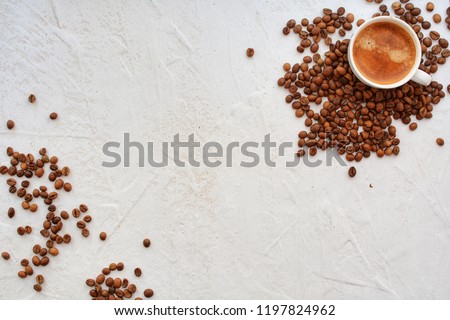 Coffee cup placed to the coffee beans. On the white table in day light. From the top.