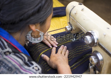 Unidentified H\'mong woman making clothes by sewing machine nearby her house. The Hmong are an Asian ethnic group from the mountainous regions of China, Vietnam, Laos, and Thailand