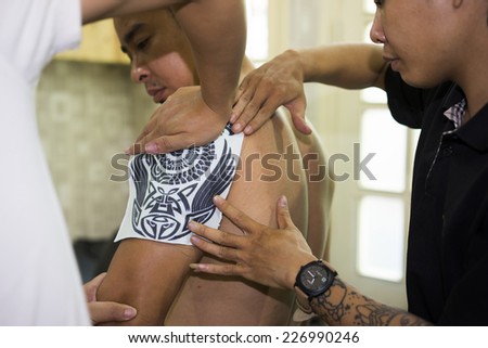 Hanoi, Vietnam - Oct 29, 2014: Tattoo artist place carbon paper on a man arm before making tattoo. This process is to print shapes on the arm