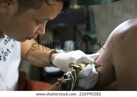 Hanoi, Vietnam - Oct 29, 2014: Tattoo artist makes a tattoo on a man arm. Focus on artist face.