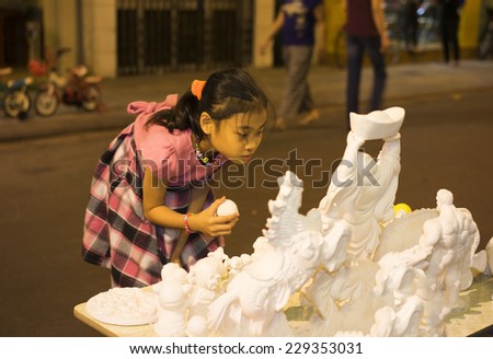 Hanoi, Vietnam - Nov 2, 2014: Child chooses clear plaster figurine before painting with color ink and brush on Ma May street, old quarter of Hanoi