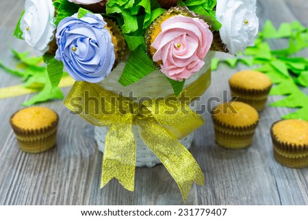 Flower bouquet of cupcakes, and other cupcakes on ground. Focus on cupcake rose flower on basket