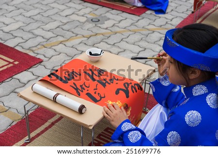 Hanoi, Vietnam - Feb 7, 2015: School children in traditional dress Ao Dai learning with calligraphy at Vietnamese lunar New Year celebrating fair day organized at Vinschool, Minh Khai, Hanoi