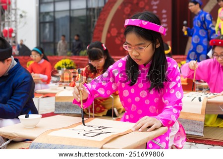 Hanoi, Vietnam - Feb 7, 2015: School children in traditional dress Ao Dai learning with calligraphy at Vietnamese lunar New Year celebrating fair day organized at Vinschool, Minh Khai, Hanoi