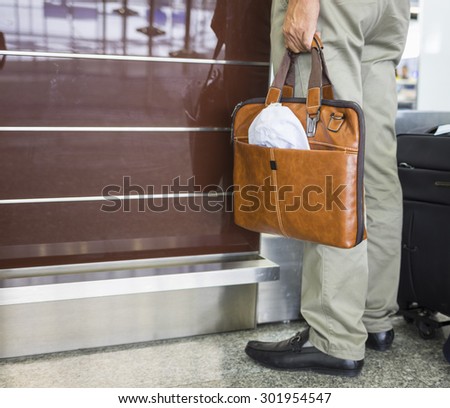 Man hand holds leather bag standing in front of airport check-in desk. Concept of tourism via aviation