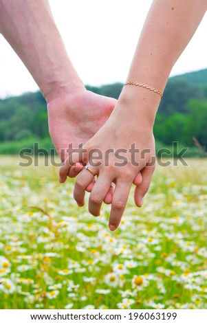 Close-up of joined hands against the background of chamomile field