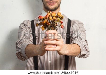 Young beautiful man in hat standing with small dry roses in his hands on white grunge background