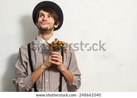 Young beautiful man in hat standing with small dry roses in his hands on white grunge background