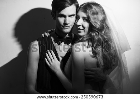 Beautiful wedding couple standing beside on white wall background. Hug each other. Black and white portrait