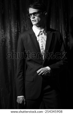 Handsome young man in business suit stay on drapes background. Black and white portrait.