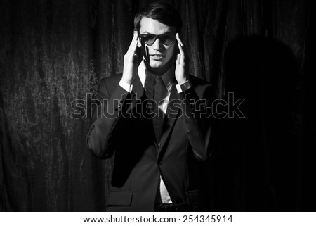 Handsome young man in business suit stay on drapes background. Holding glasses. Black and white portrait.