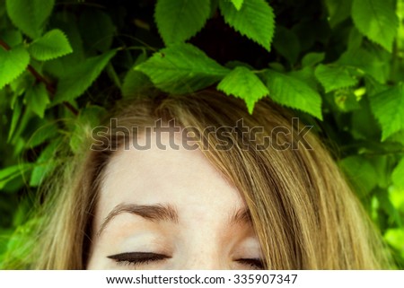 close up of female closed eyes with foliage above her head. soft focus.