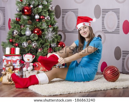 Girl sitting on the carpet beside the Christmas tree. Girl puts a big new year socks
