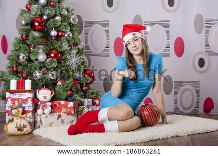 Girl sitting on the carpet beside the Christmas tree. Next is a big red Christmas ball. Girl dreams