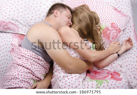 Young couple sleeping in bed under the belt blanket. Guy hugging a girl back. The girl's face is hidden by hair. Photo made at the top