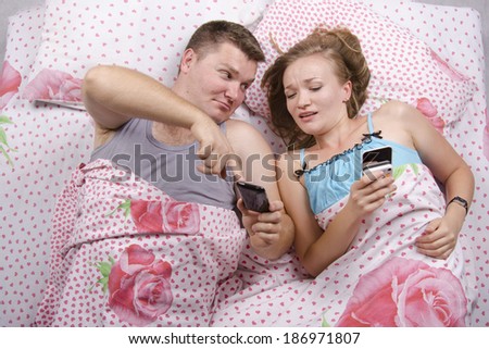 Young couple lying in bed. Everyone in my hand phone. The guy shows something interesting girl in your phone. Photo made at the top