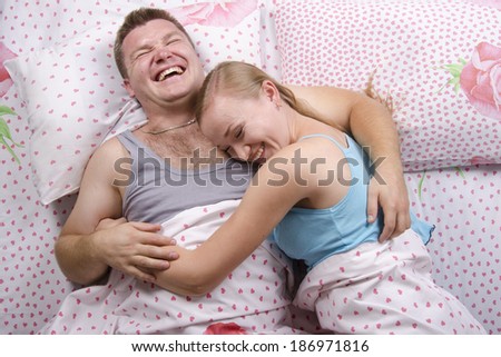 Young couple sleeping in bed under the belt blanket. The girl lay down on the guy\'s shoulder. About happily laugh. Photo made at the top