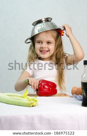 Girl playing in a cook. Carried away by the game she put on a colander on his head. Studio. Light background.
