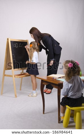 Girl and educator draw on the Board of geometric shapes. Also on the foreground there is a table at which sat the other girl who looks carefully at the Board