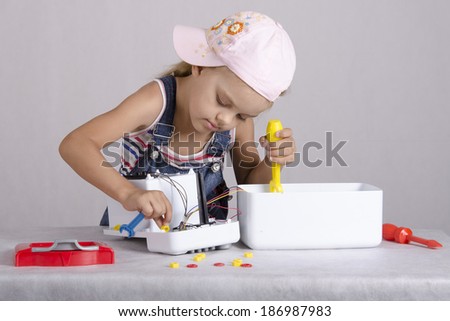 Girl playing in the repairer and repairs toy microwave. Girl enthusiastically digging inside the device, cheat nut, in the other hand he holds a wrench