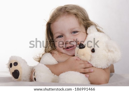 Two-year-old girl lies. Teddy bear sitting in front of her. Girl hugging a bear. Studio light background