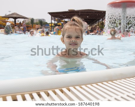 Four-year-old girl bathes in a public pool. The girl came up to the edge of the pool and looks into the frame. Summer day.l