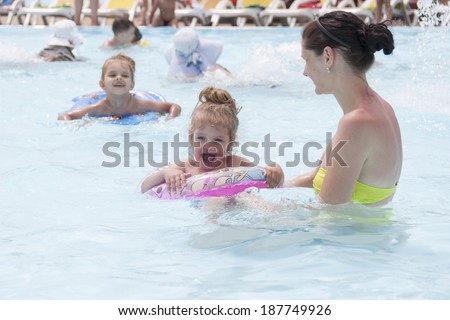 A mother and two daughters are swimming in a public pool. Daughters of the two and four years. Daughter swim in circles