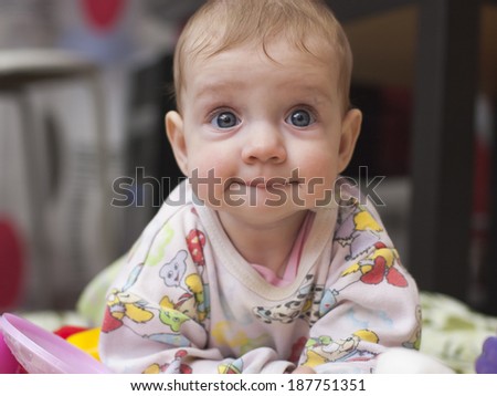 A six-month baby lying leaning on the handle with a funny look looking into the camera, and pursed his lips. home furnishings