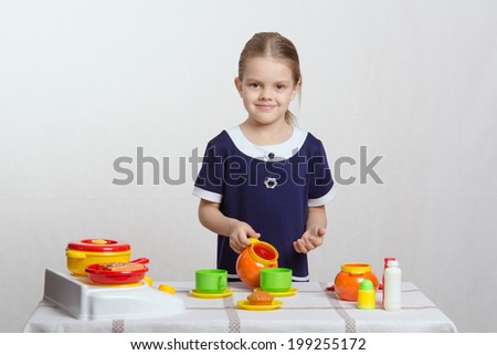 Five year old girl plays children\'s dishes at a table covered with a cloth