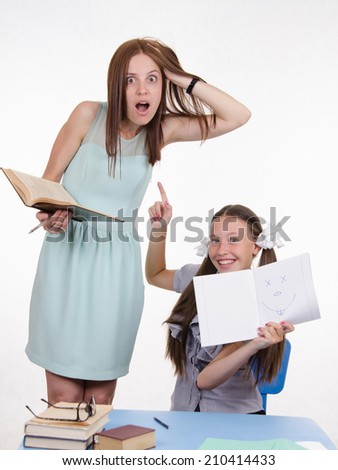 Teacher standing at desk behind which sits student who drew a funny face in a notebook