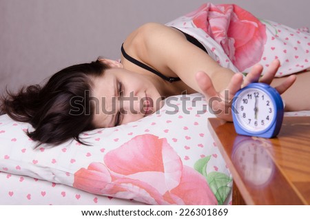 Woman asleep in bed, standing beside an alarm clock on the table, the places on the six o\'clock
