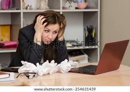 The girl at computer with a bunch of crumpled sheets paper