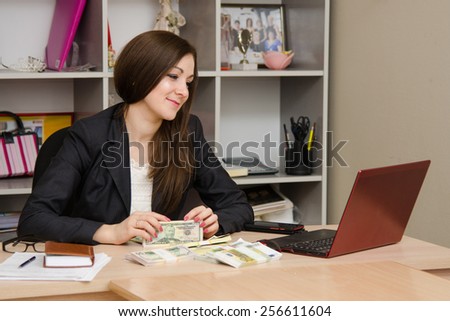 Joyful Girl sitting a desk with pile of money and looking at computer