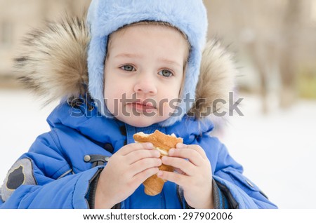 The three-year girl is outside in the winter eating a muffin