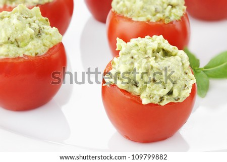 Stuffed Tomatoes filled with a pesto and avocado mixture. Extreme shallow depth of field with selective focus on tomato in foreground.