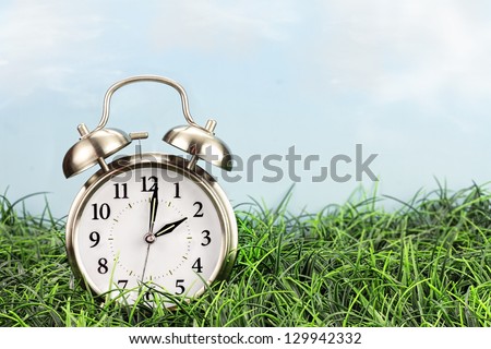 Set your clocks back with this clock in grass against a bright sky. Daylight saving time concept.